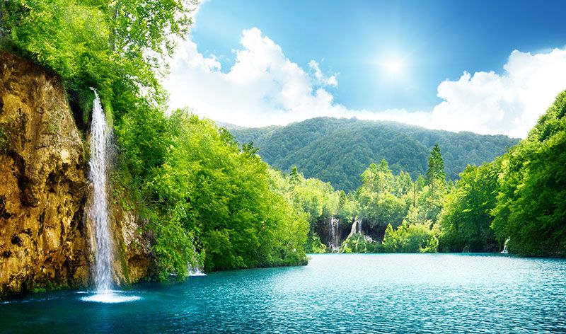 عکس با کیفیت بالا طبیعت زیبای آبشار و دریاچه با درختان و کوه های زیبا در تابستان و آسمان آبی یا دانلود عکس با کیفیت طبیعت بکر و کوه و جنگل و چشم انداز