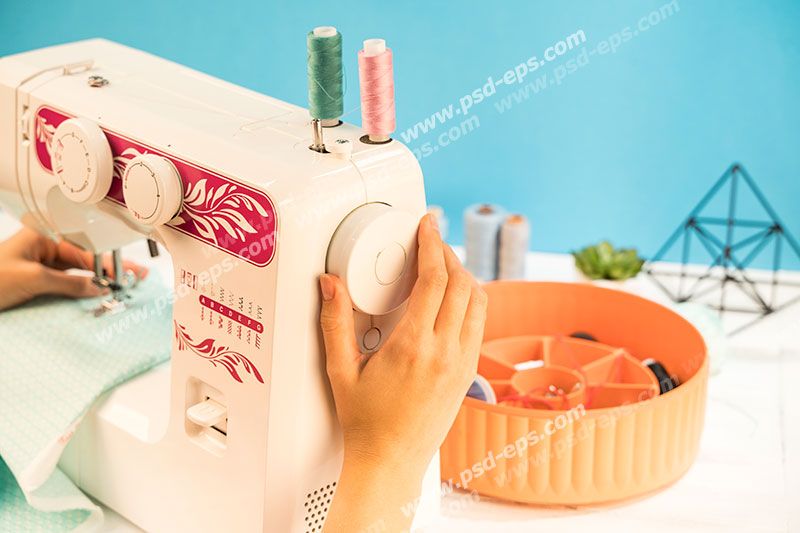 عکس با کیفیت چرخ خیاطی در کنار جعبه ابزار خیاطی در حال دوخت پارچه فیروزه ای رنگ