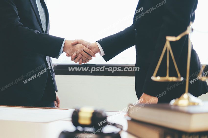 عکس با کیفیت میز قاضی یا وکیل با ترازوی عدالت بر روی آن با زمینه دو آقا با کت و شلوار در حال دست دادن